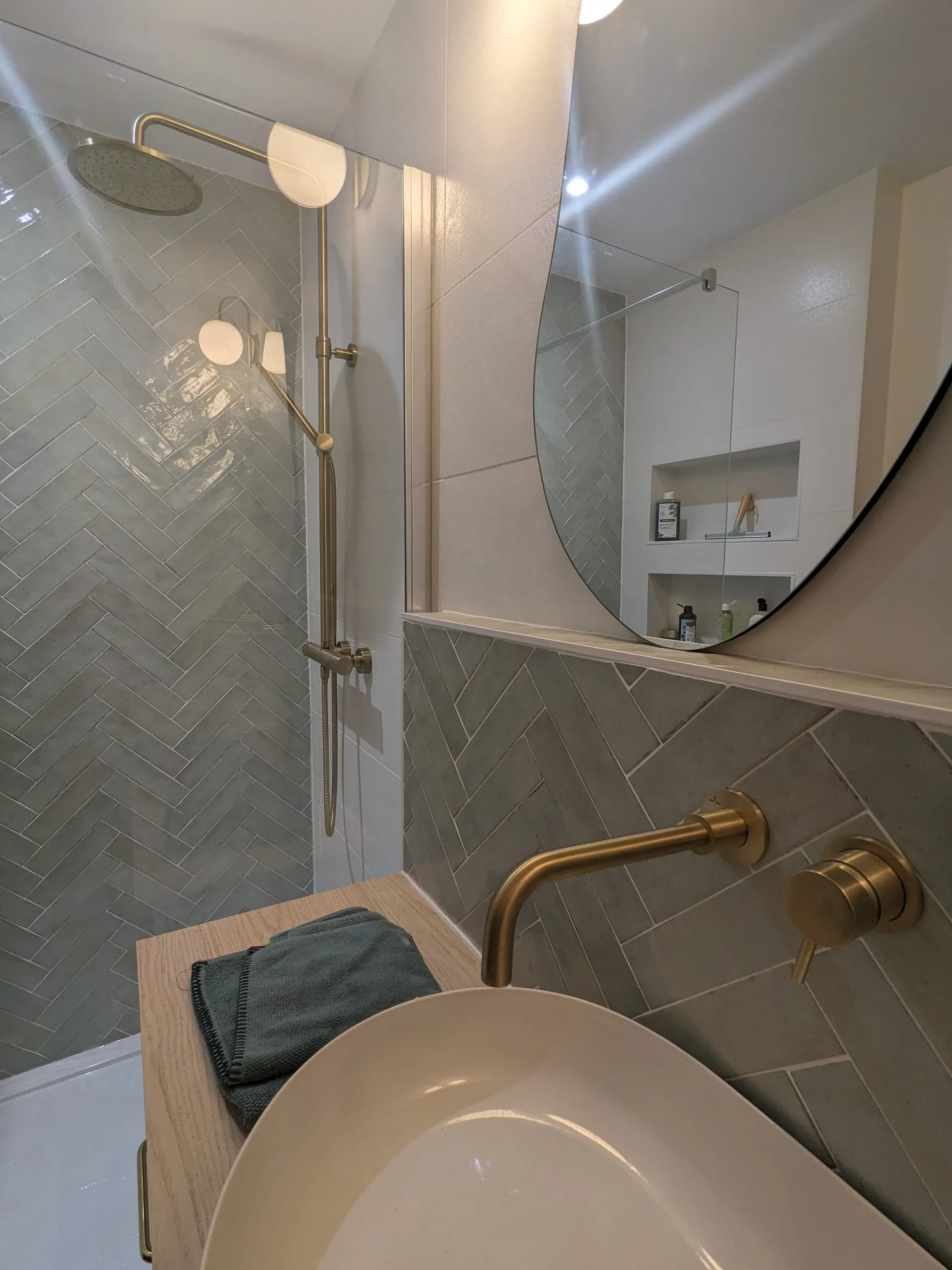 Douche ouverte avec carrelage gris en chevrons, robinetterie en laiton et miroir ovale
