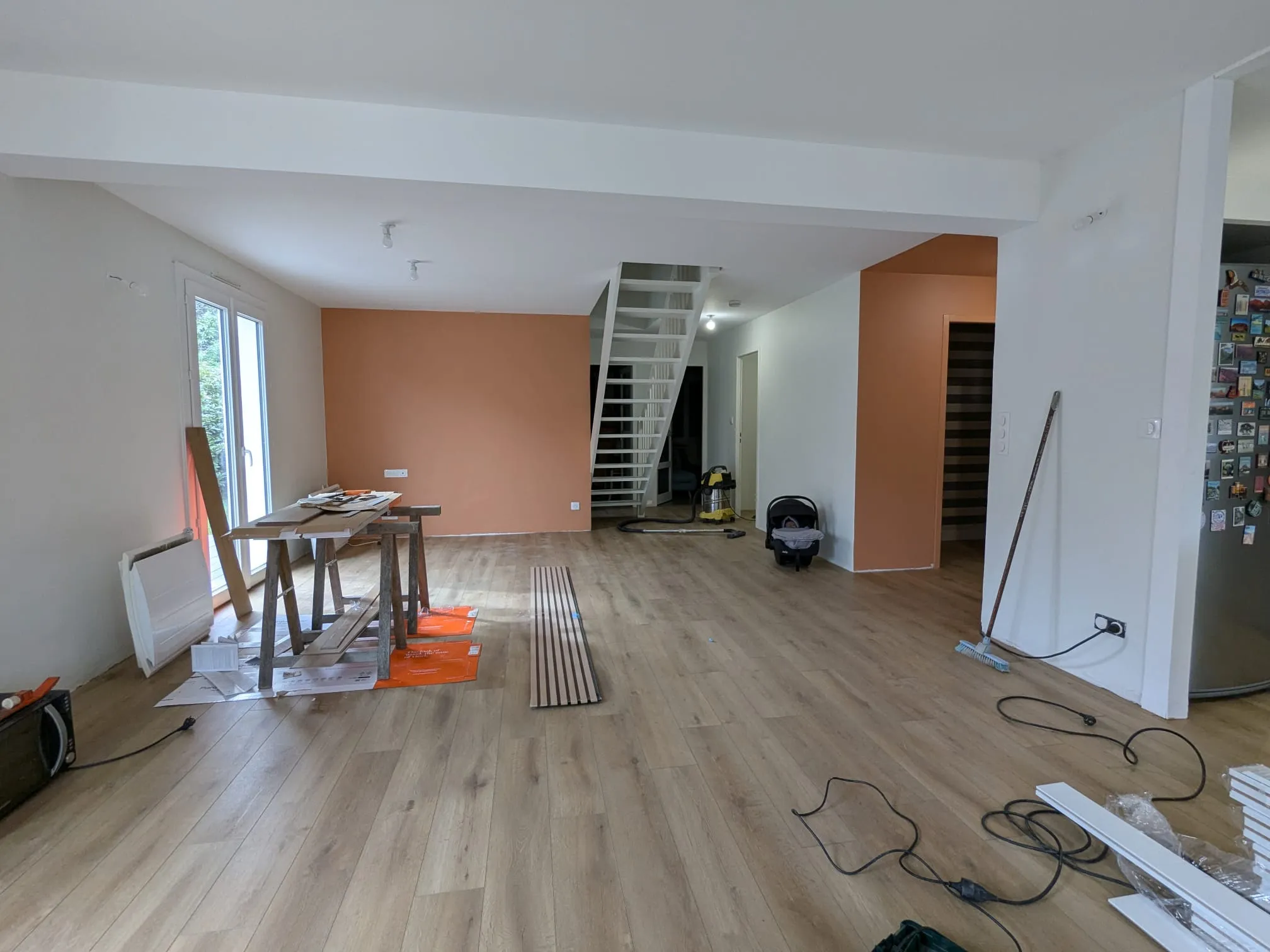 Pièce de vie en fin de chantier avec sol bois, murs blancs, aplats terre cuite et escalier ouvert