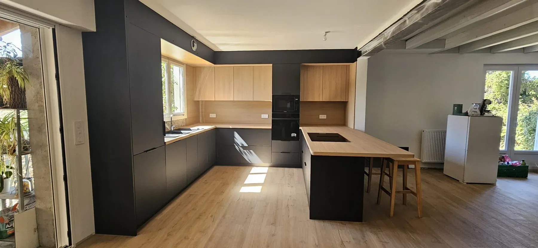 Cuisine rénovée noire et bois dans une pièce lumineuse