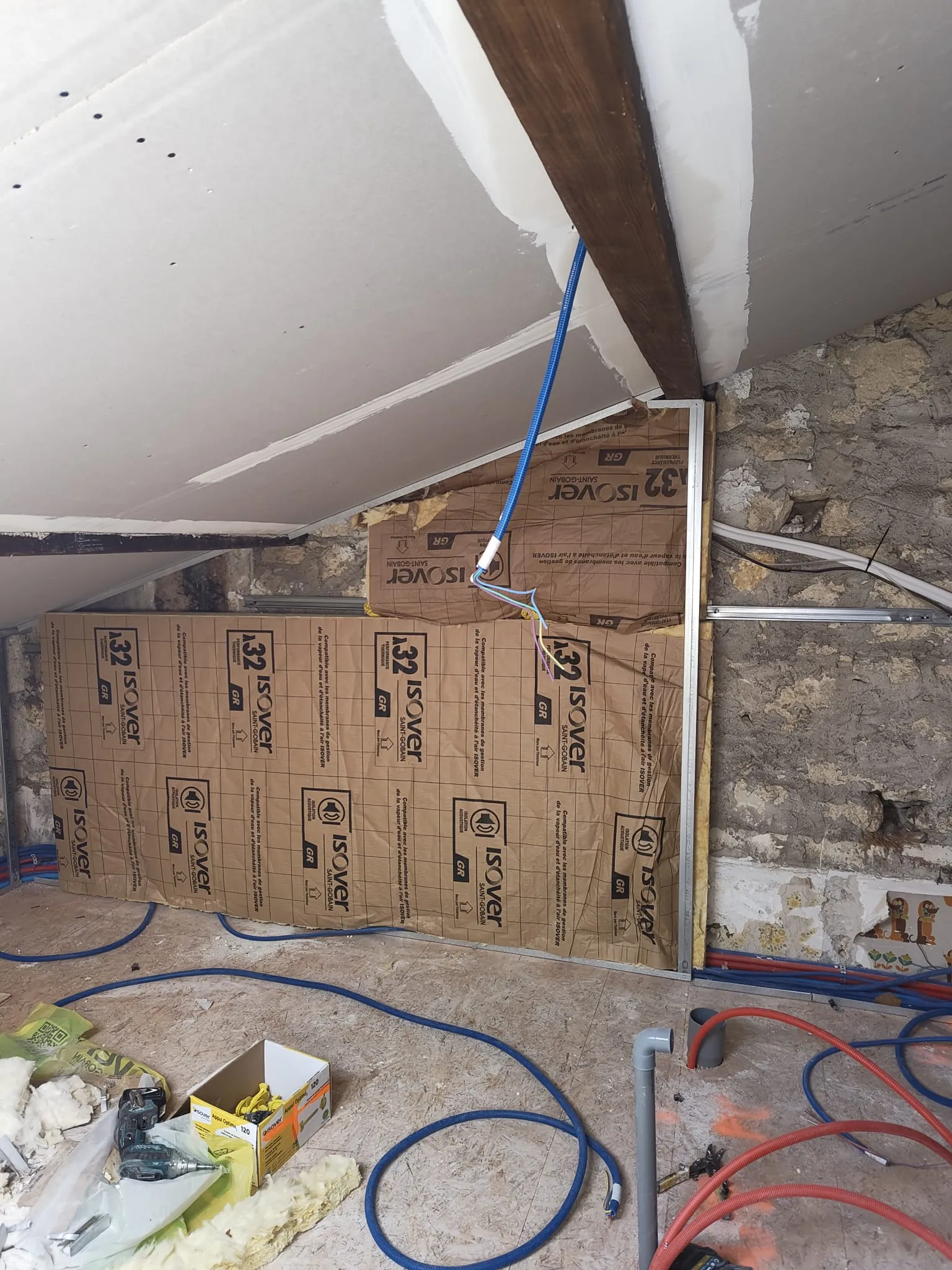 Isolation et plaques de plâtre posées sous toiture avec mur en pierre et gaines électriques apparentes