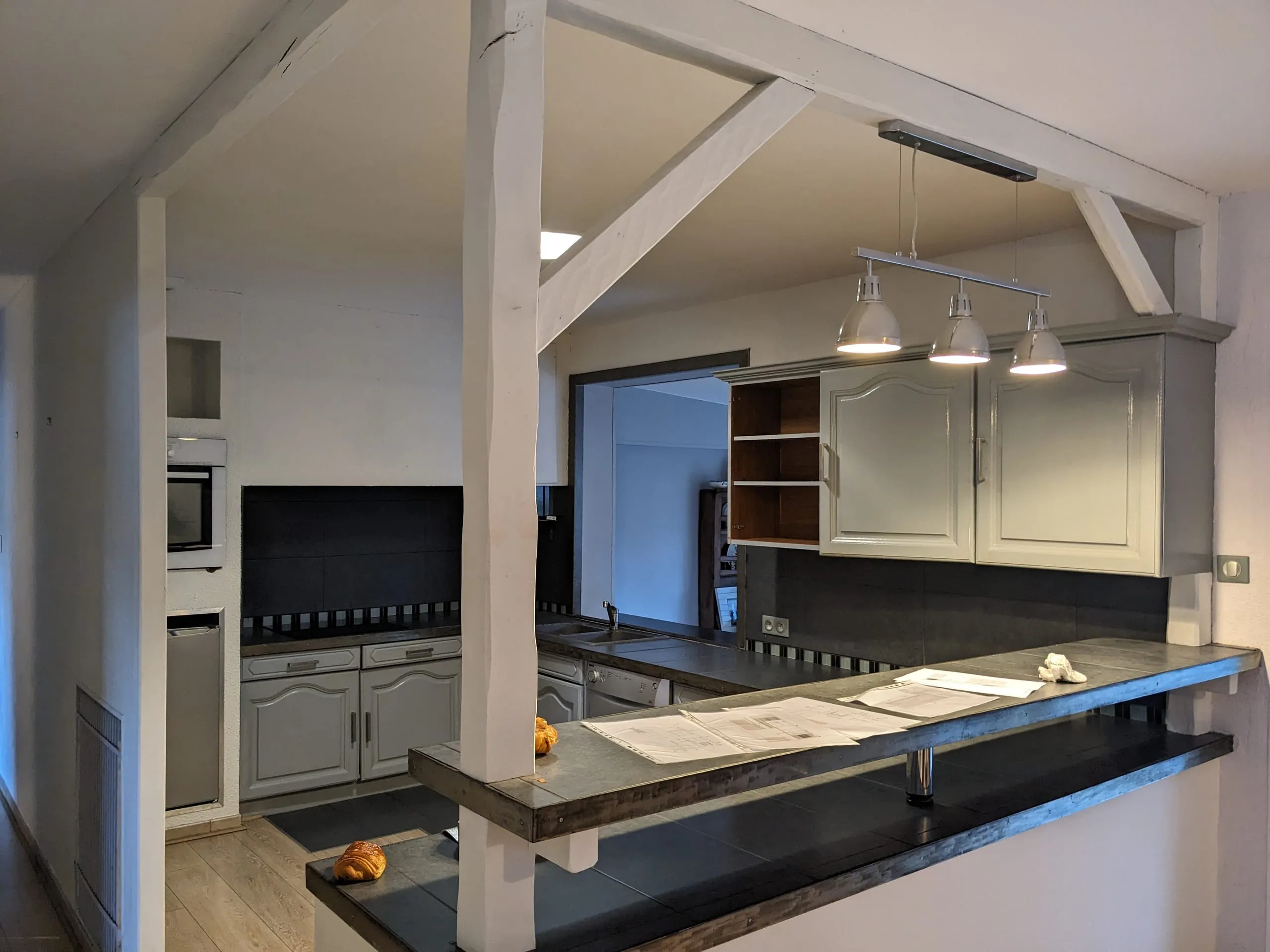 Cuisine avant rénovation avec meubles blancs et gris, plan de travail noir et cloison légère